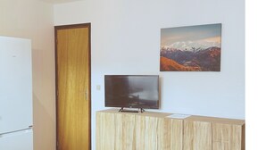 Quarto pequeno com um armário de madeira, uma televisão em cima e uma pintura na parede.