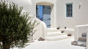 Un edificio blanco con una escalera que lleva a una puerta, una ventana pequeña y un árbol.