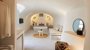Un dormitorio moderno con una cama, mesitas de noche, una pequeña mesa redonda, un sofá, un espejo y una toalla colgada.