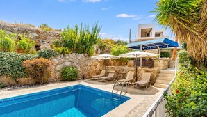 A swimming pool with lounge chairs and umbrellas, surrounded by greenery and stone walls. - The Bridge Villa by Ezoria Villas (Paphos)