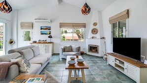 A spacious living area with a sofa, a coffee table, a TV, and a fireplace. There are decorative items and a view of the outside. - The Bridge Villa by Ezoria Villas (Paphos)