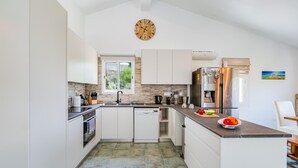 A modern kitchen with white cabinetry, a stone backsplash, a built-in oven, a dishwasher, and a stainless steel refrigerator. - The Bridge Villa by Ezoria Villas (Paphos)