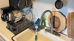 Eine Küche mit Holzausstattung, einer Kaffeemaschine, einem Wasserkocher, einer Pfanne, einem Topf, einem Geschirrständer, einem Wasserhahn und einer Seifenspender.