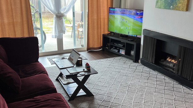 Ein Wohnzimmer mit rotem Sofa, Fernseher, Kamin und Blick durch eine Glastür.