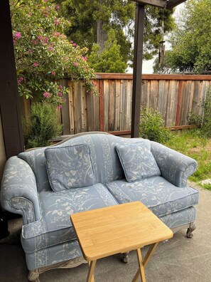 A blue floral-patterned sofa with wooden legs, a small wooden table, and a wooden fence in the background.