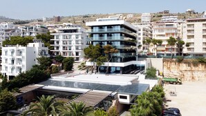 A modern multi-story building with balconies, a rooftop terrace, and a parking area. - Mango Luxury Resorts (Sarandë)