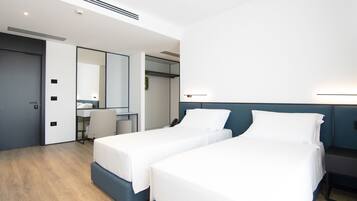 A modern hotel room with two beds, a desk, and a mirror.