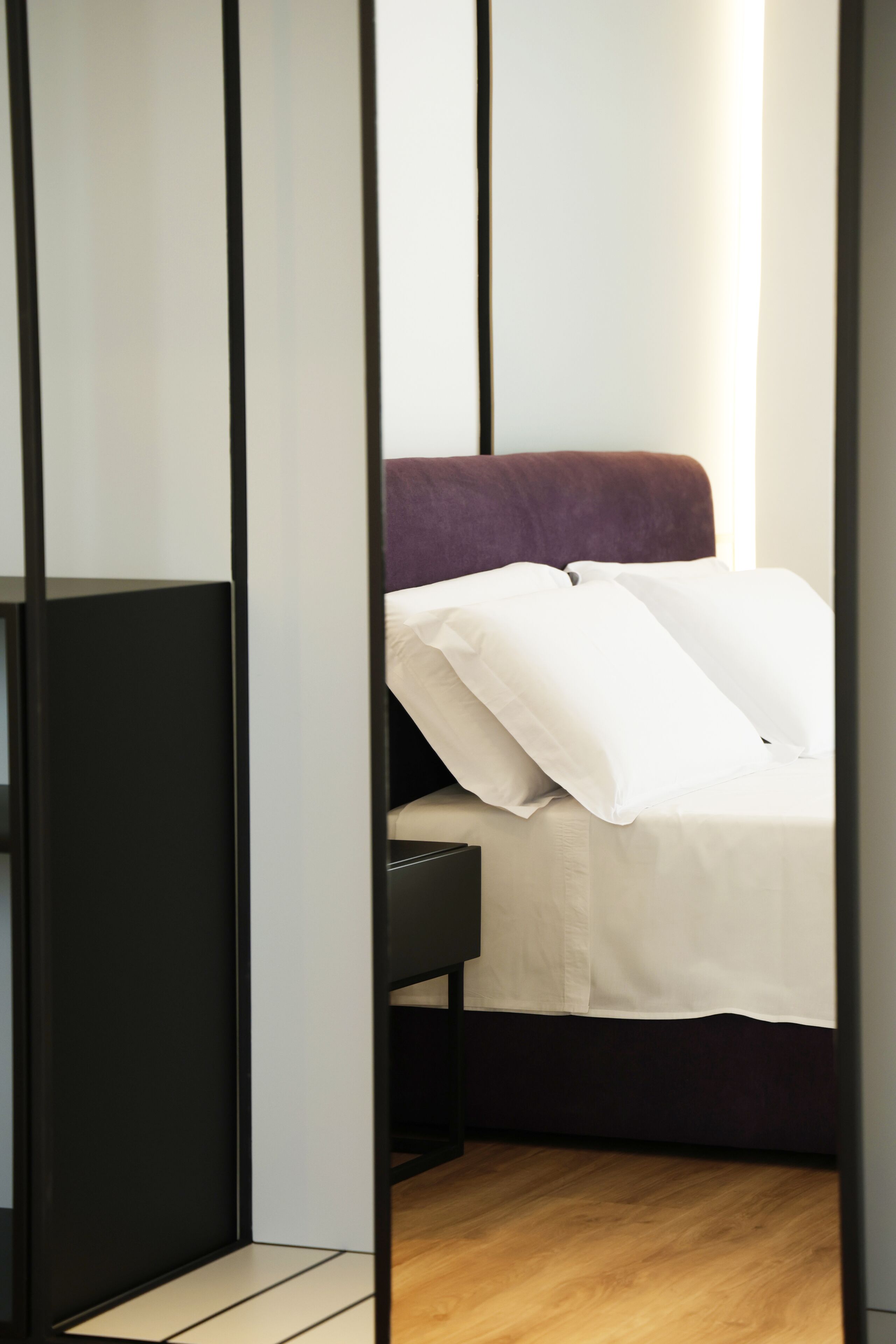 A modern bedroom with a bed, a black headboard, and a wooden floor.