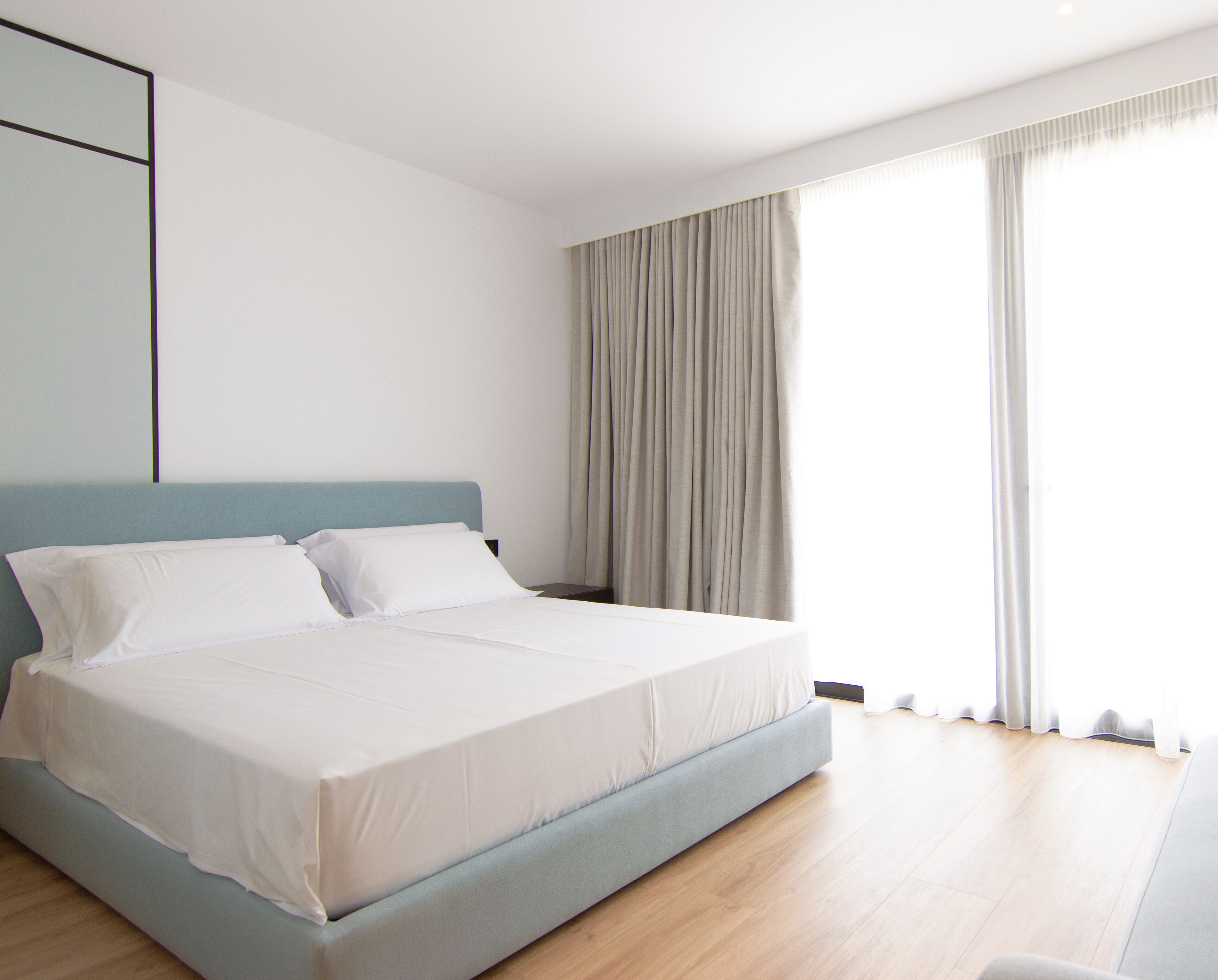 A modern bedroom with a large bed, a nightstand, and a window with curtains.