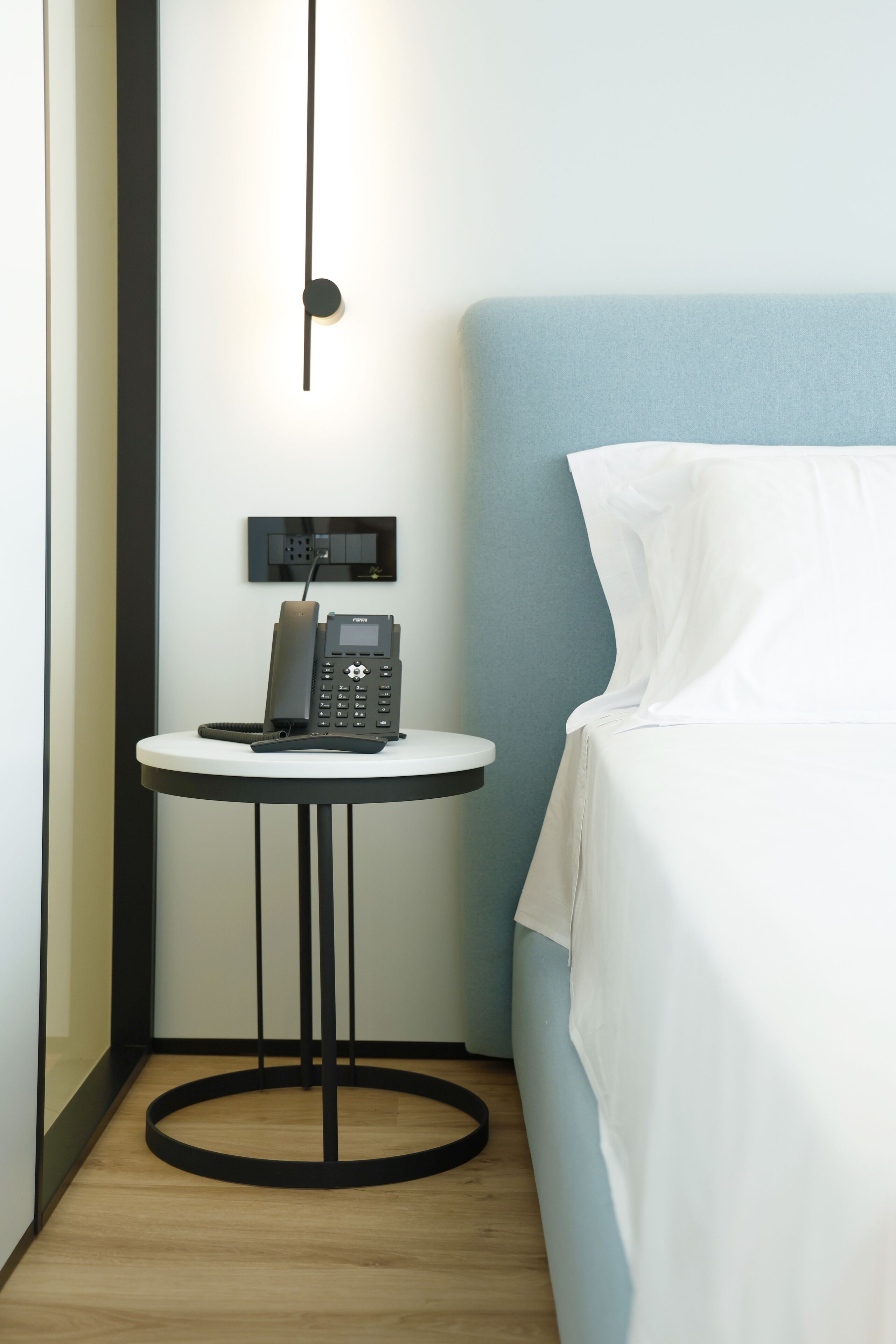 Una habitación de hotel con una cama, una mesa redonda con un teléfono y una lámpara fijada a la pared.