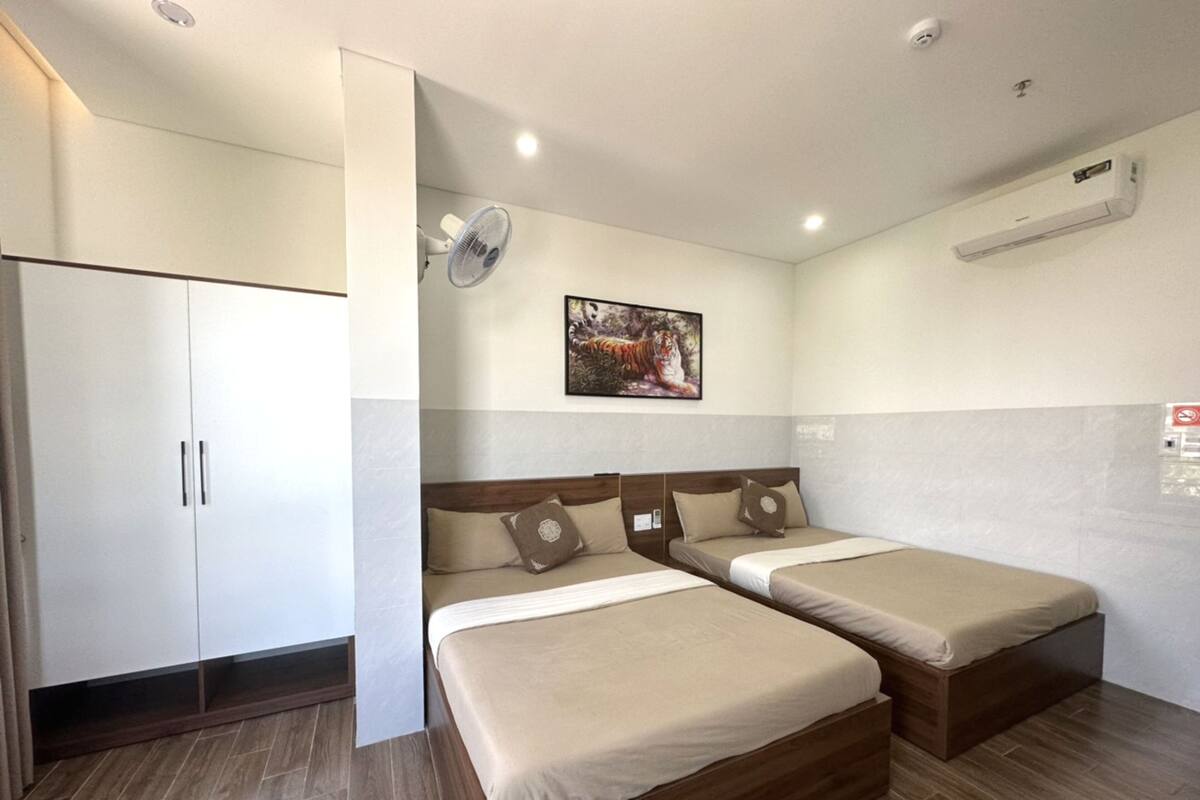 A hotel room with two single beds, a wardrobe, a ceiling fan, an air conditioning unit, and a framed picture on the wall.