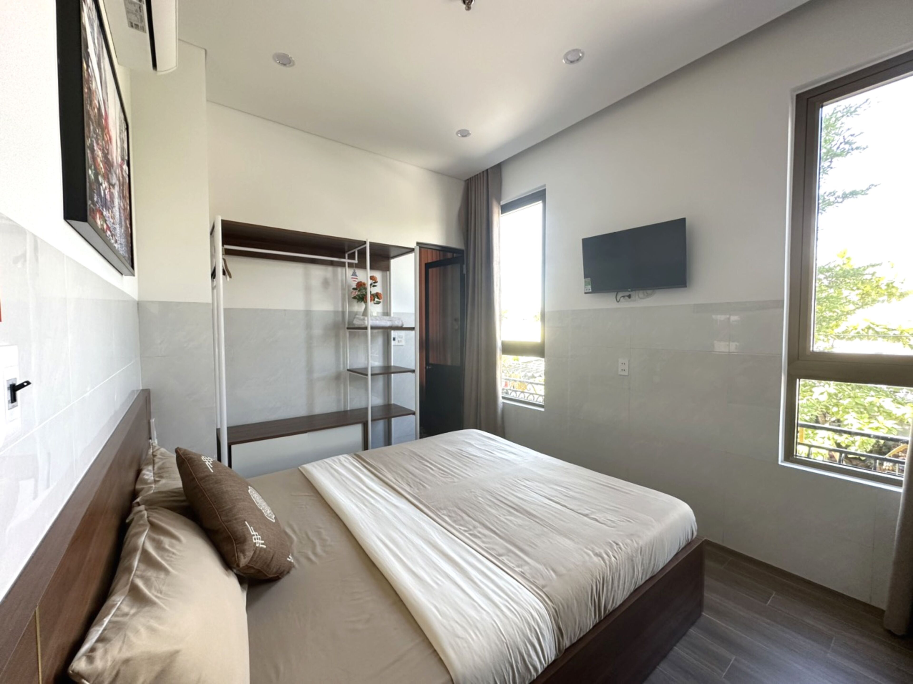 Un dormitorio moderno con cama, armario, televisor y ventana con vistas.