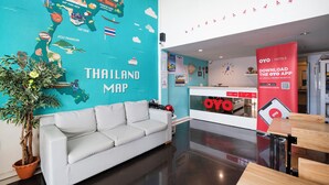 A hotel lobby with a teal wall featuring a Thailand map, a white sofa, a wooden table, and a red OYO app promotion banner. - OYO 1193 Huynh Gia Hotel (Da Nang)