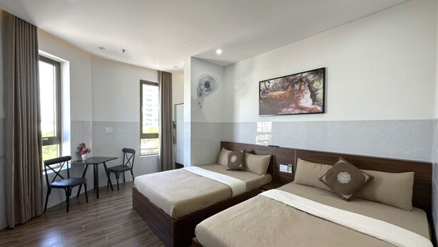 A hotel room with two beds, a dining table with chairs, a window with curtains, and a wall-mounted air conditioner. - OYO 1193 Huynh Gia Hotel (Da Nang)