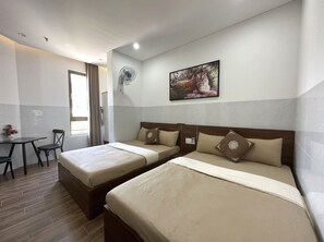 Une chambre d’hôtel avec deux lits, un bureau, une chaise, un ventilateur et un tableau au mur.