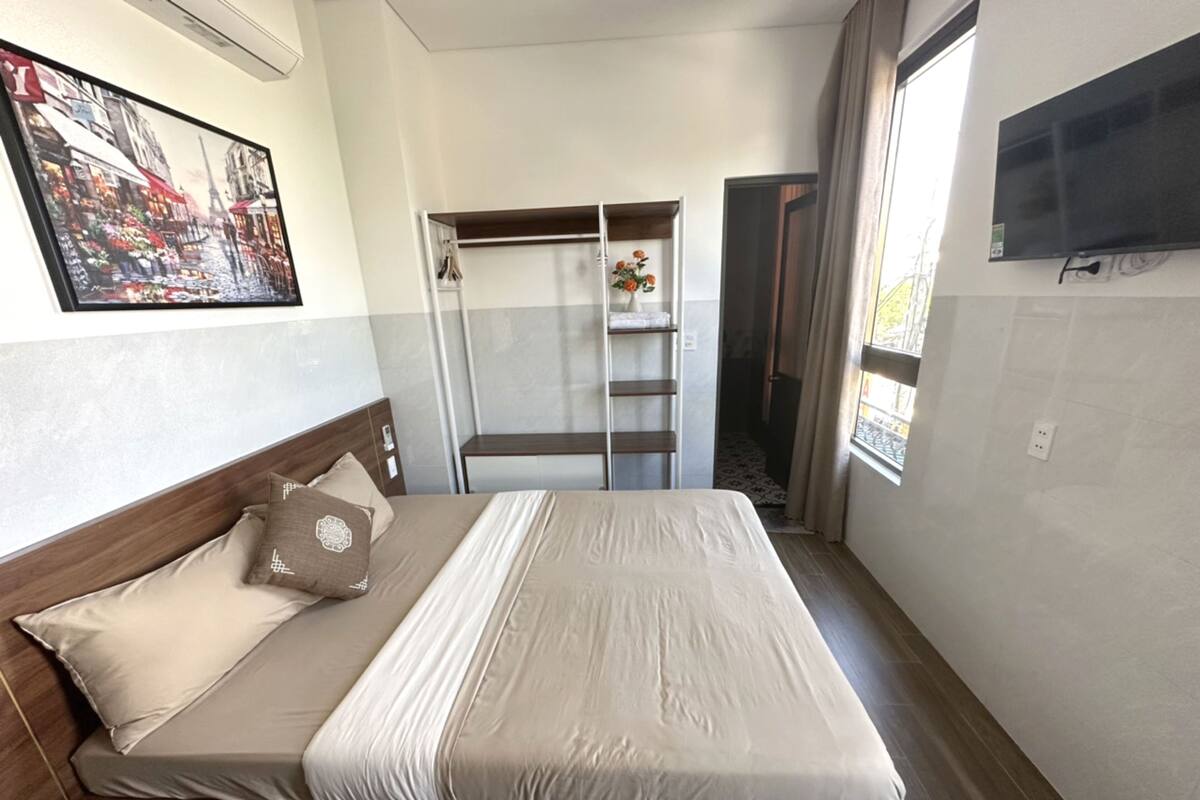 A hotel room with a bed, a wardrobe, a TV, and a painting on the wall.