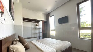 A bedroom with a bed, a TV mounted on the wall, and a window with a view of greenery. - OYO 1193 Huynh Gia Hotel (Da Nang)