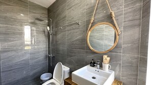 A modern bathroom with a marble wall, a white toilet, a sink with a wooden countertop, and a round mirror. - OYO 1193 Huynh Gia Hotel (Da Nang)