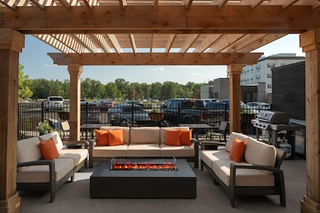 An outdoor patio with a wooden pergola, a fire pit, and a sofa set.