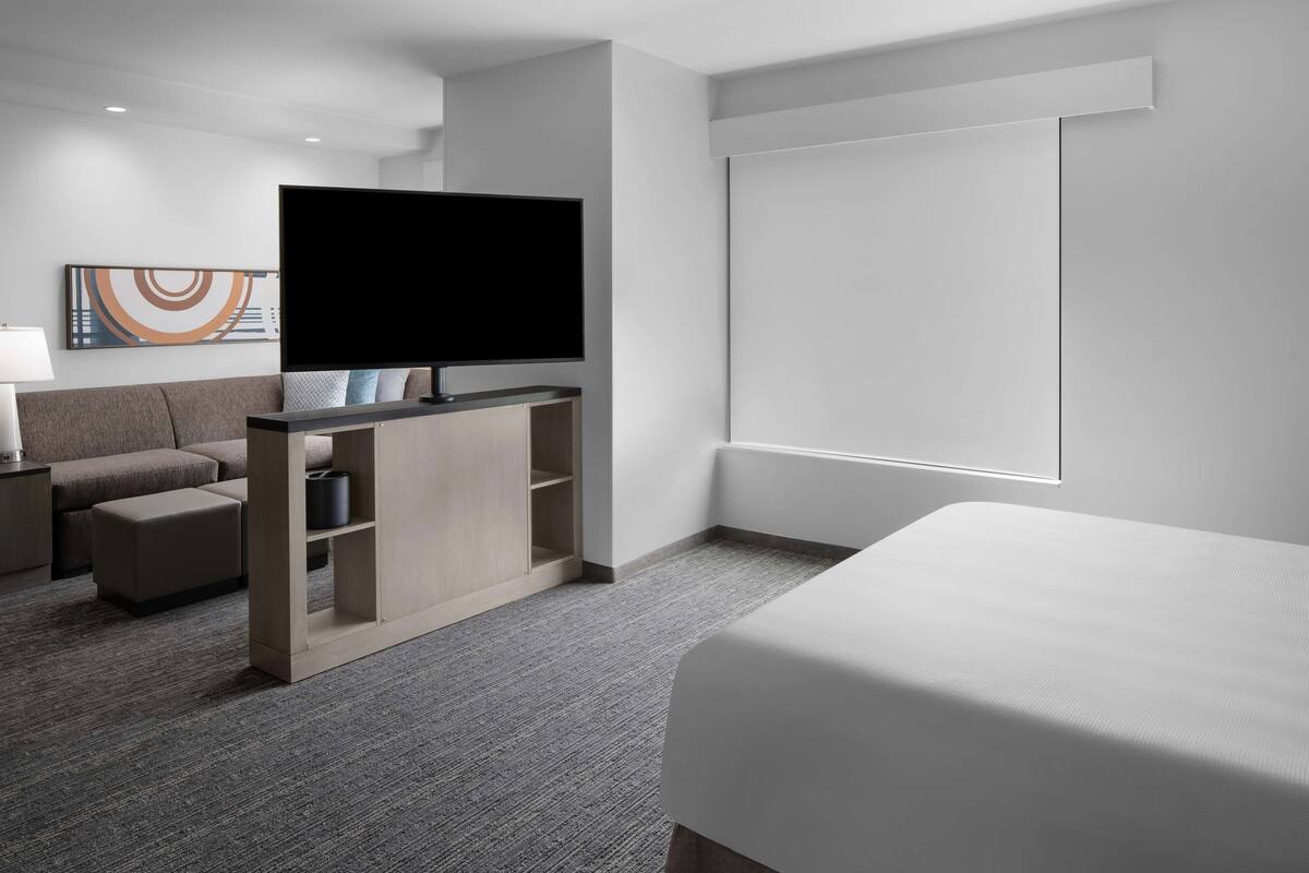 Ein modernes Hotelzimmer mit einem großen Bett, einem Flachbildfernseher, einer Couch und einem kleinen Tisch.