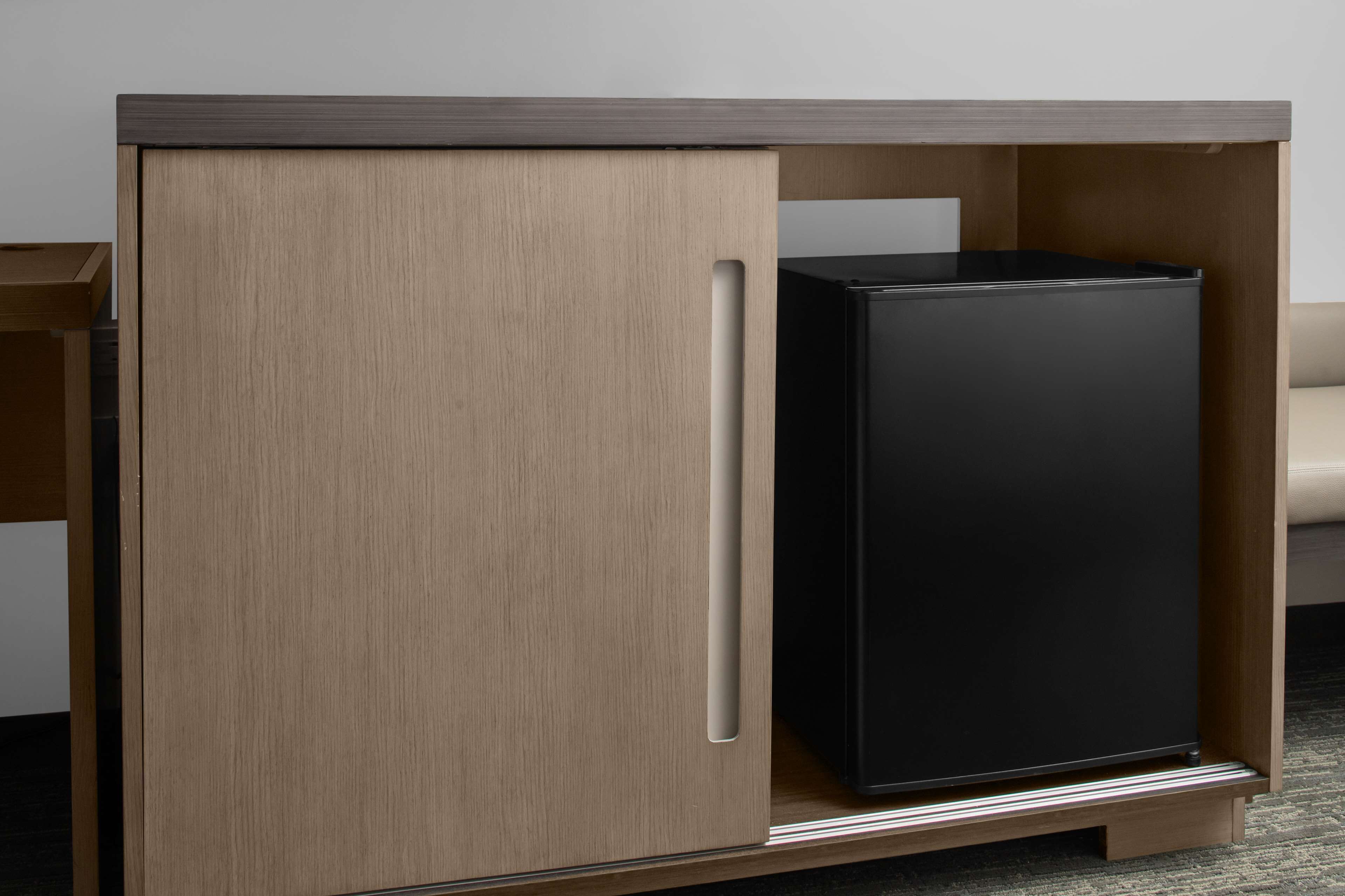 A modern, built-in black refrigerator in a wooden cabinet with a handle, set against a plain wall.