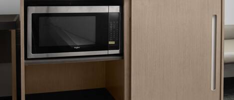A compact kitchenette with a microwave, a small shelf with glasses, and a wooden cabinet.