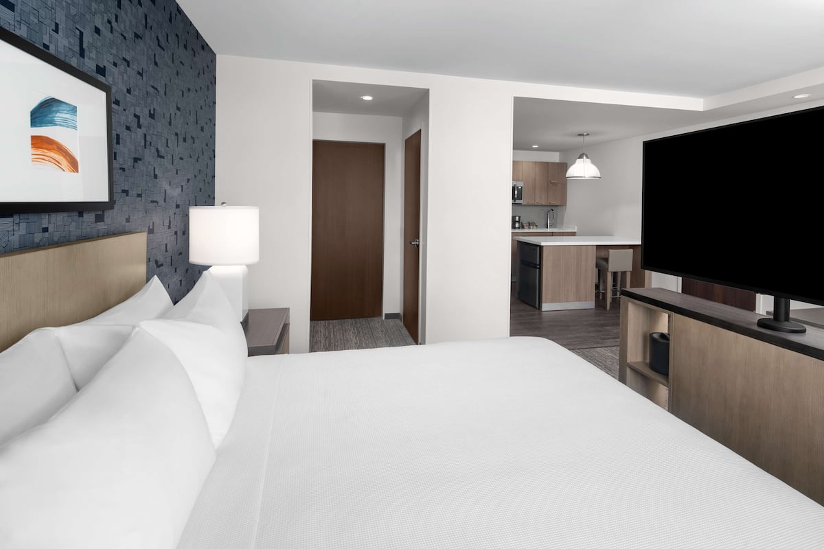 Ein Hotelzimmer mit einem großen Bett, einem Fernseher, einem Schreibtisch und einer Küchenzeile.