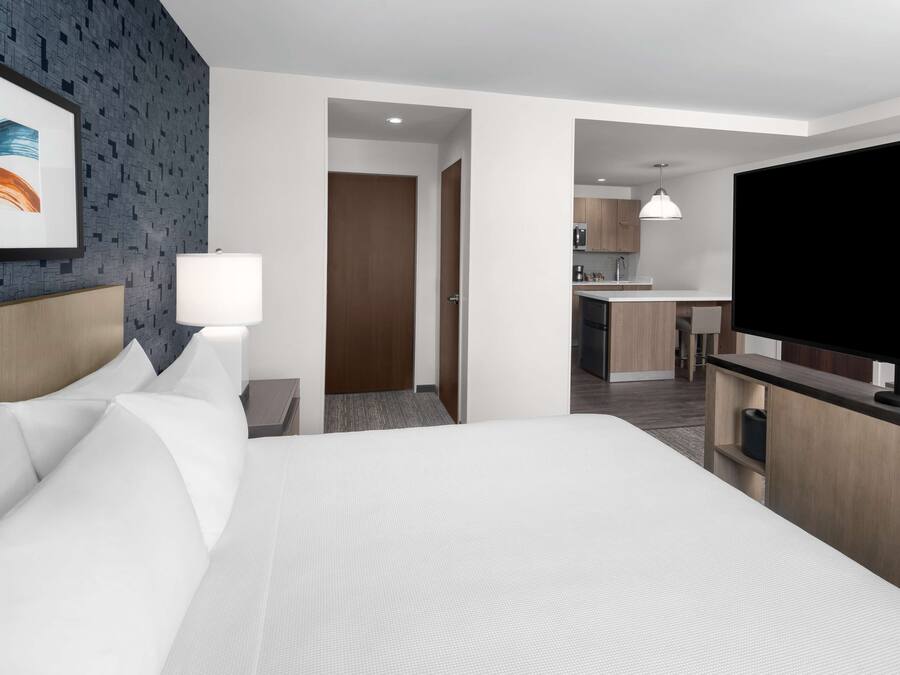 A hotel room with a large bed, a TV, a desk, and a kitchenette.