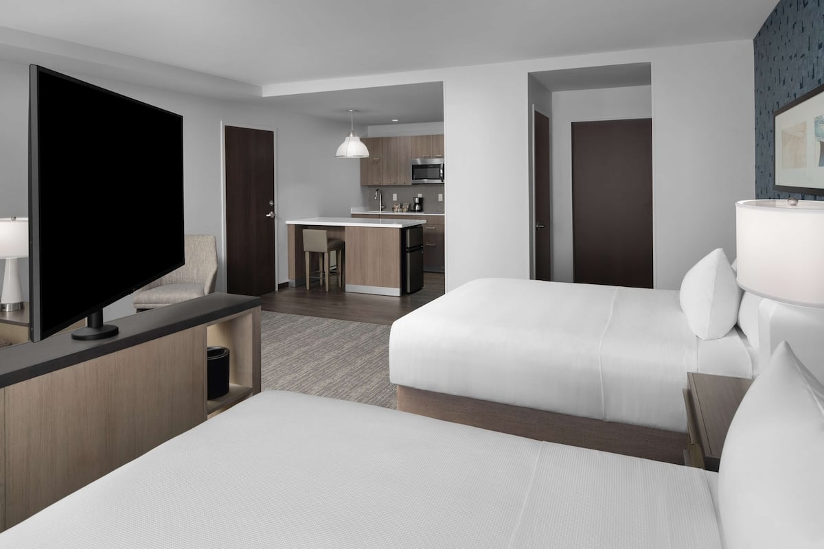 Ein Hotelzimmer mit zwei Betten, einem Fernseher, einem Schreibtisch und einer Küchenzeile.