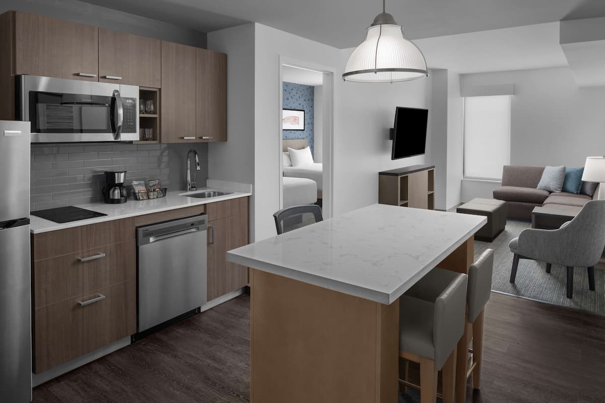 Eine moderne Küche mit Einbau-Mikrowelle, Geschirrspüler und einer großzügigen Kücheninsel. Es gibt einen Essbereich mit Tisch und Stühlen sowie ein Wohnzimmer mit Sofa und Fernseher.