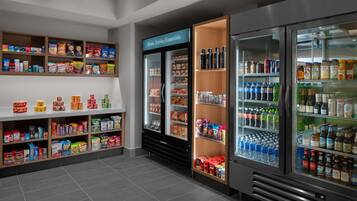 A self-service beverage and snack kiosk with refrigerated and non-refrigerated sections, shelves stocked with various snacks and drinks, and a clear sign indicating the kiosk's purpose.