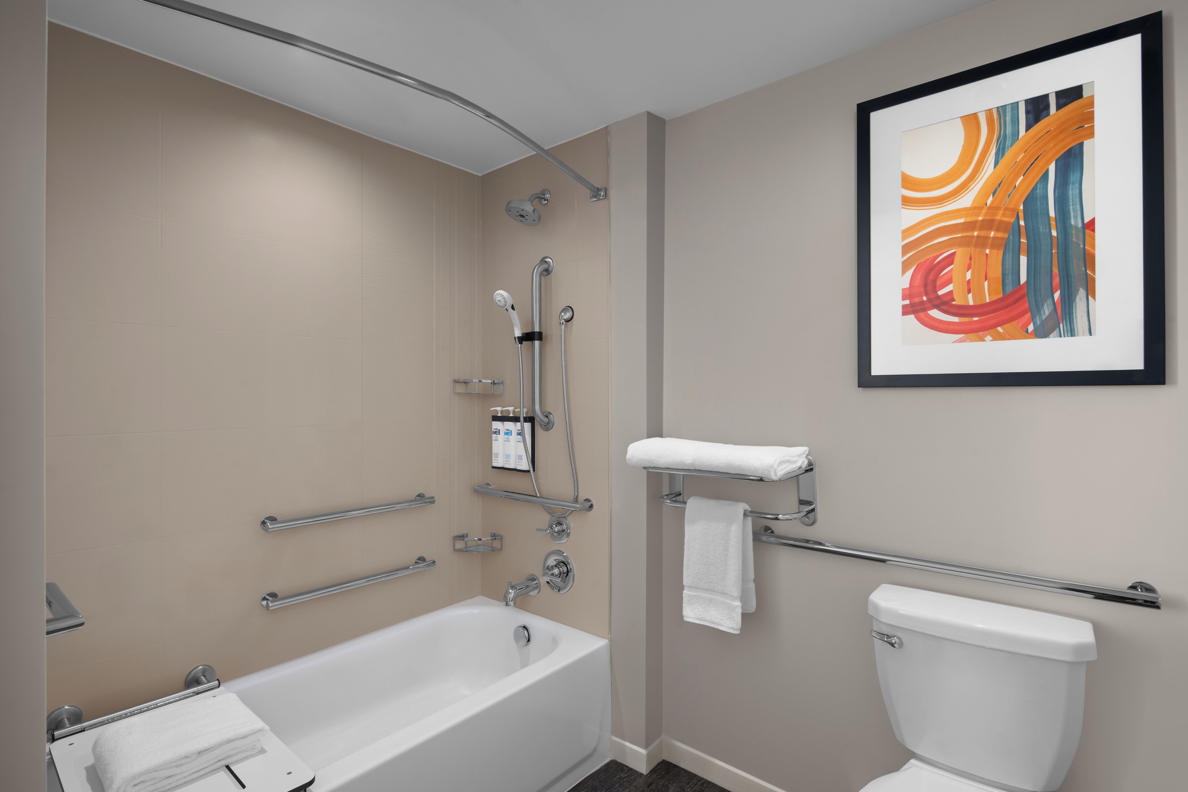 Un baño moderno con bañera, inodoro y ducha. Se observan barras de apoyo y un perchero para toallas.