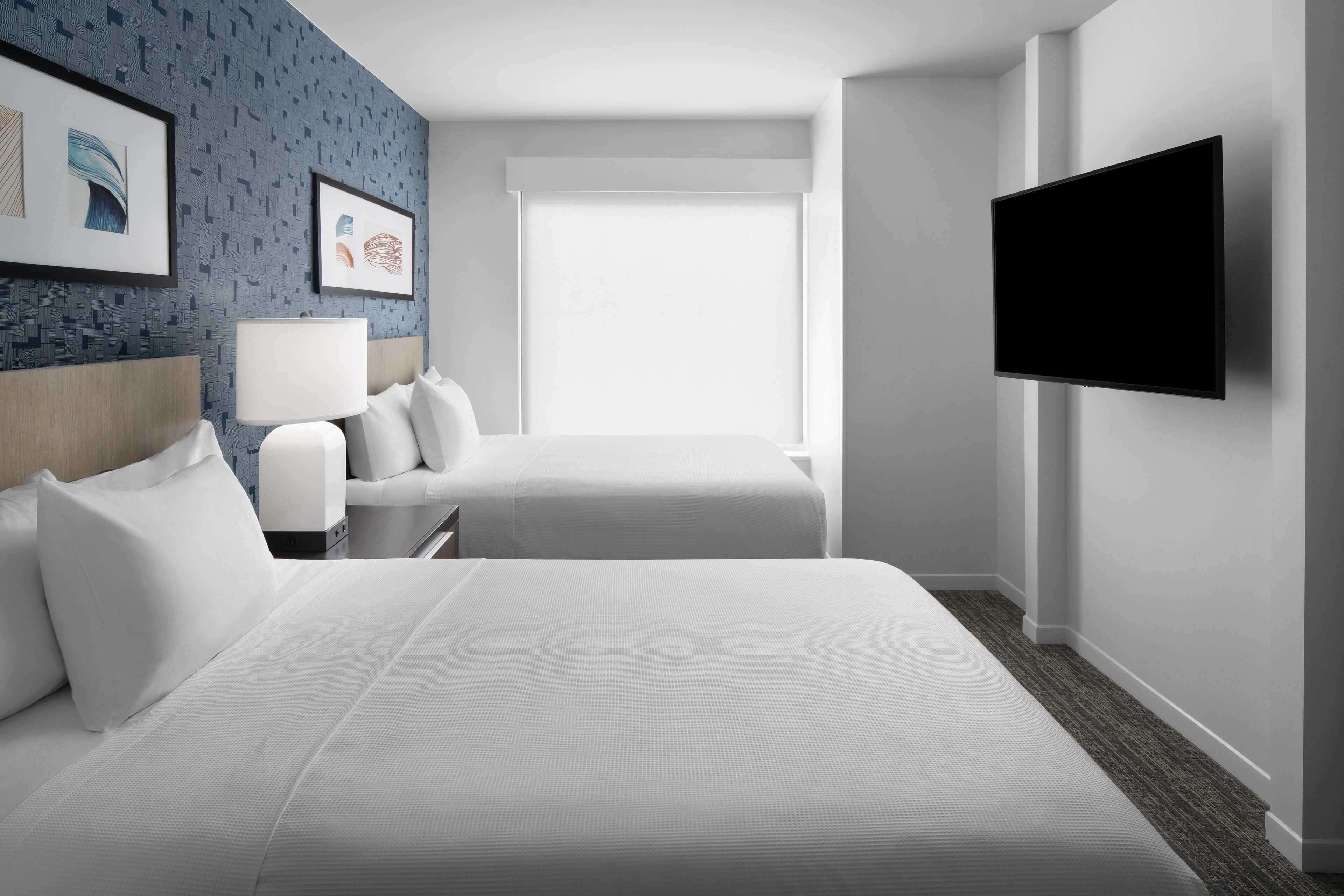 Habitación de hotel con dos camas, un televisor de pantalla plana, un ventanal y obras de arte en la pared.