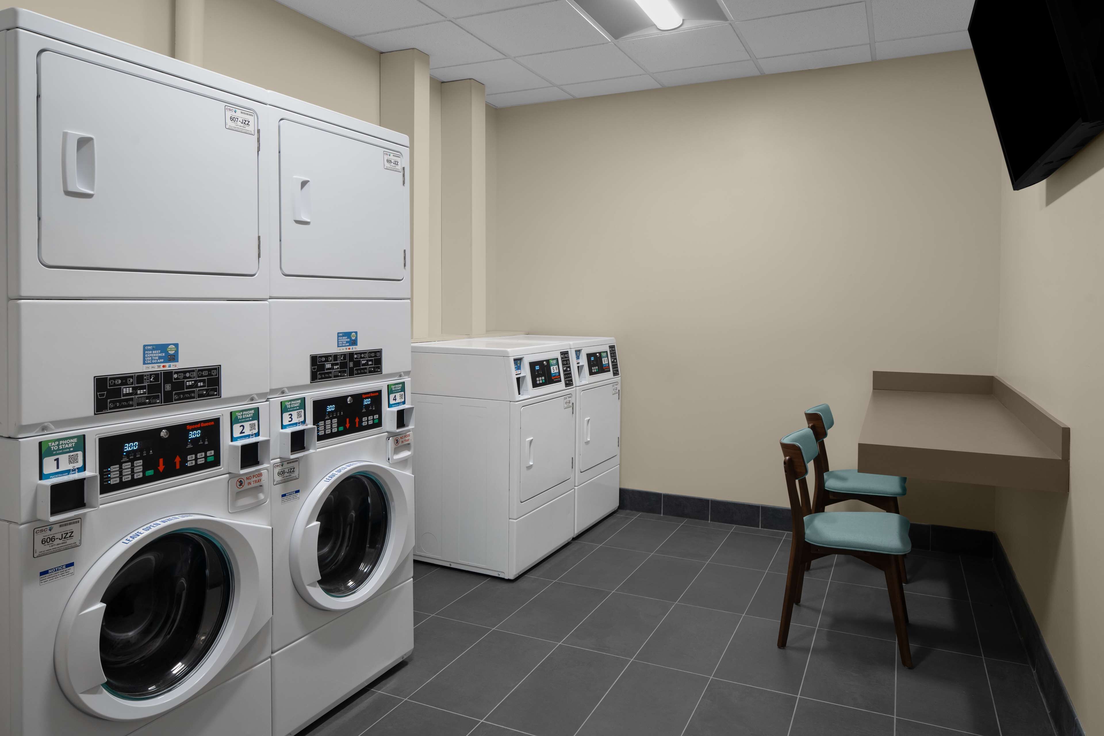 A laundry room with stacked washers and dryers, a chair, and a flat-screen TV mounted on the wall.