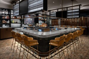 Un bar moderno con barra central, diversas opciones de asientos y una variedad de botellas y vasos en estanterías.