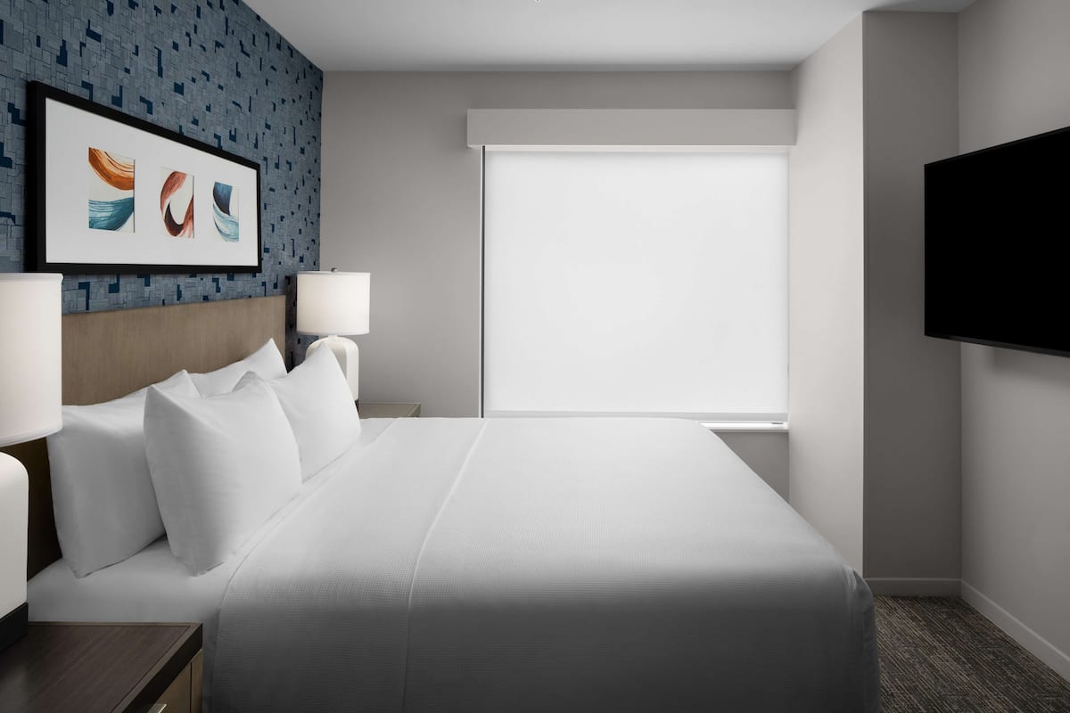 Ein Hotelzimmer mit einem großen Bett, zwei Nachttischen mit Lampen, einem an der Wand befestigten Flachbildfernseher und einem Fenster mit Blick.