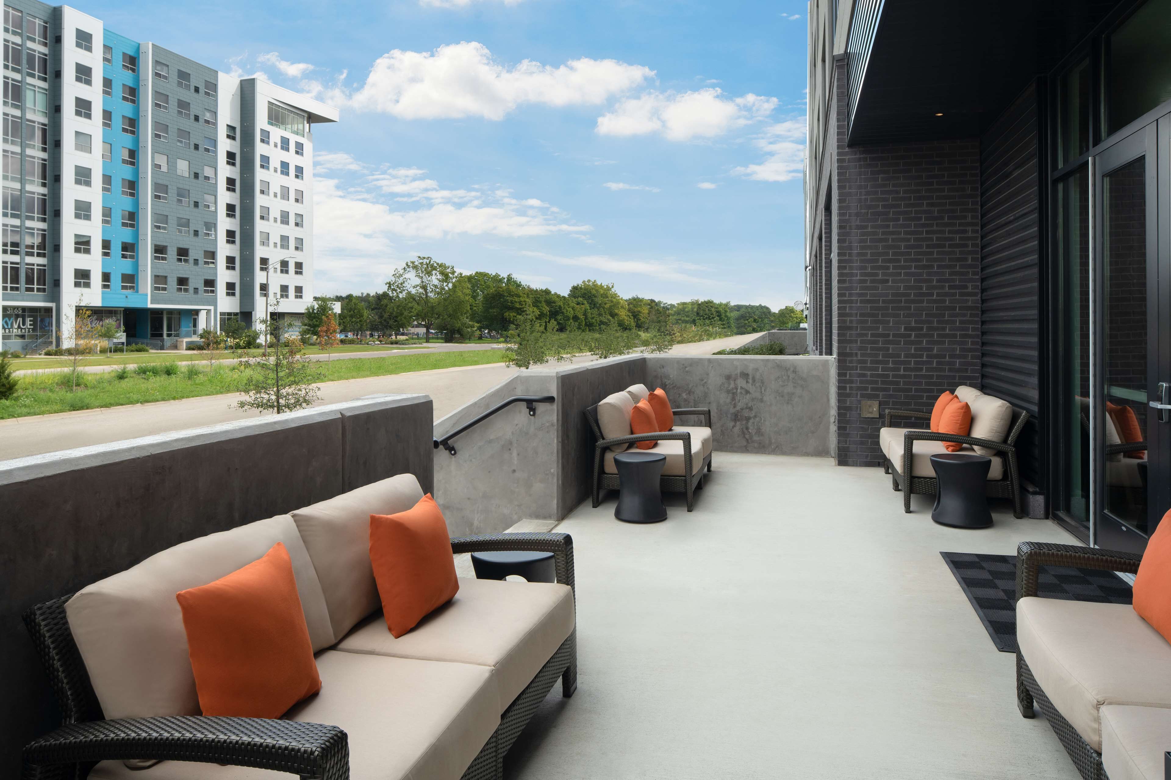 An outdoor seating area with wicker furniture and orange cushions, a concrete floor, and a view of a modern building in the background.
