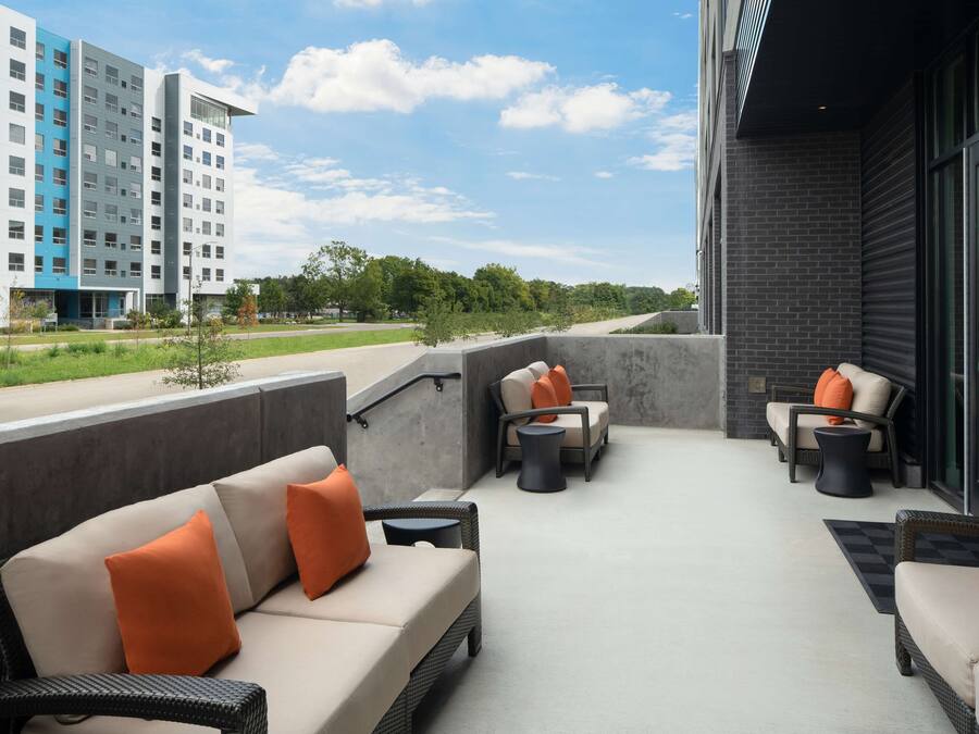 An outdoor seating area with wicker furniture and orange cushions, a concrete floor, and a view of a modern building in the background.