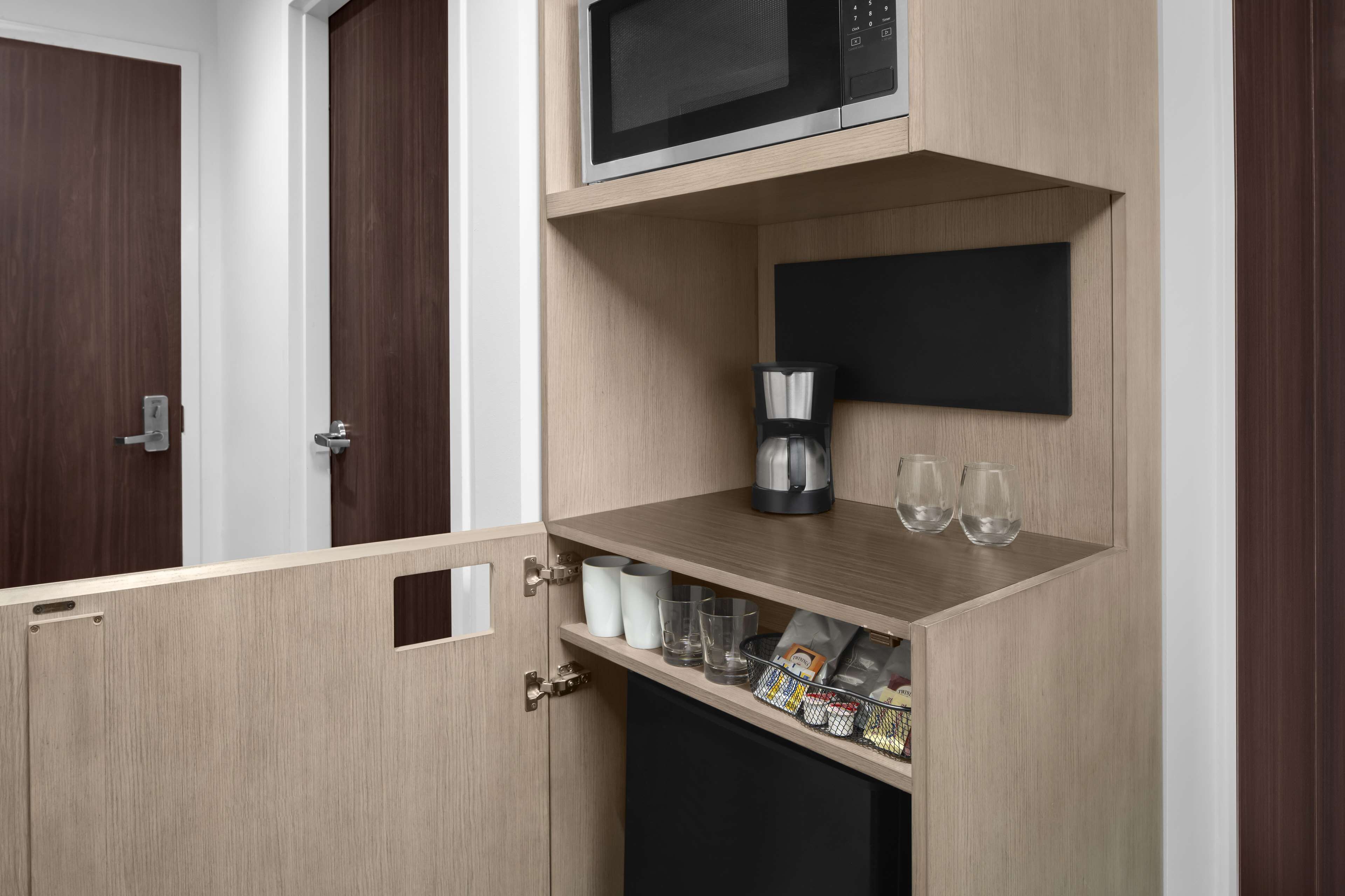 Una kitchenette compacta con microondas, cafetera y cristalería.