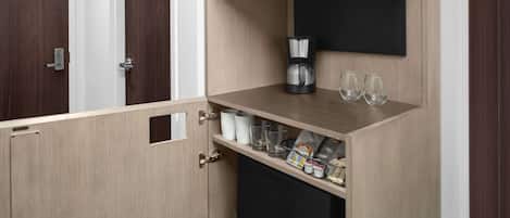 A compact kitchenette with a microwave, coffee maker, and glassware.