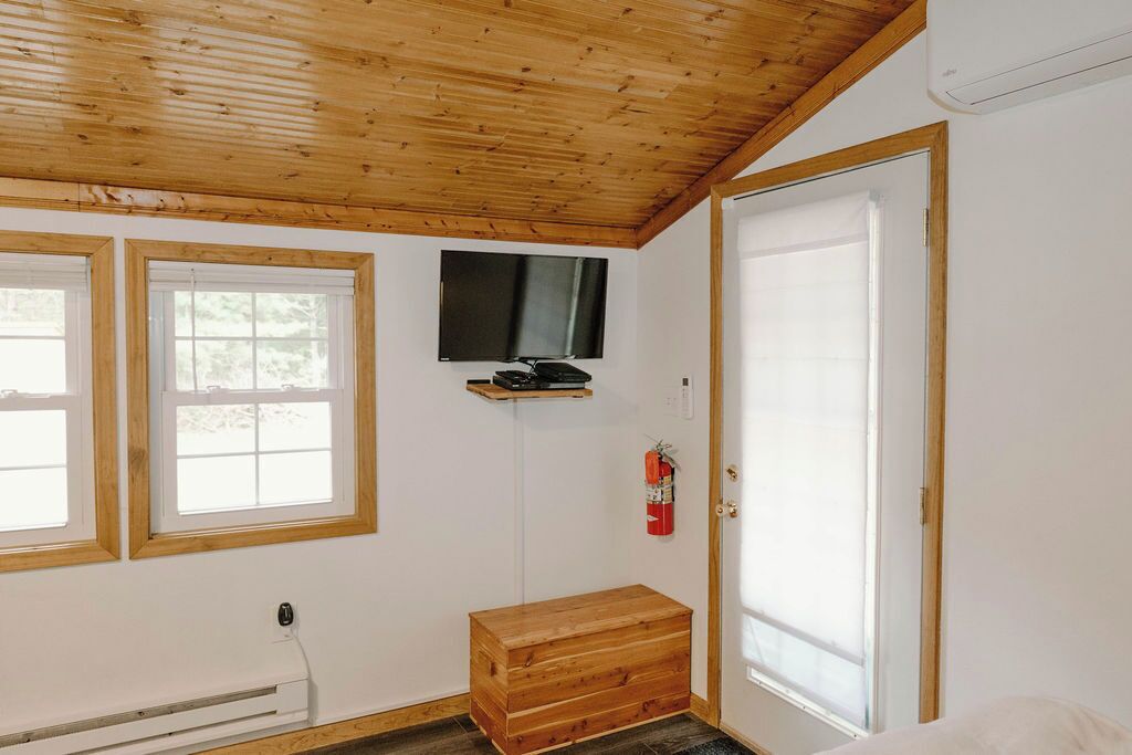 Una habitación con techo de madera, un televisor montado en la pared, un extintor y un cofre de madera.