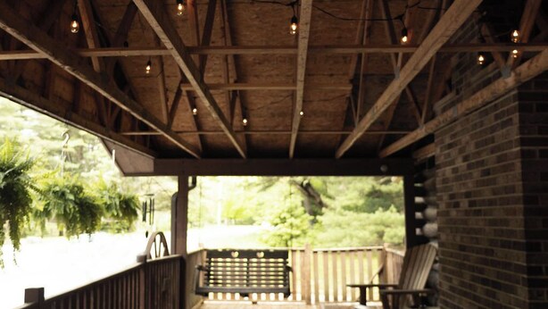 A covered deck with wooden beams, string lights, and a barbecue grill. - Remodeled Cook Forest Cabin (Clarington)