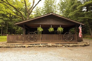 A wooden cabin with a porch, two large wheels, and an American flag. - Remodeled Cook Forest Cabin (Clarington)