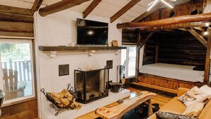 A cozy log cabin interior with a fireplace, a television mounted on the wall, and a bed with a wooden headboard. - Remodeled Cook Forest Cabin (Clarington)