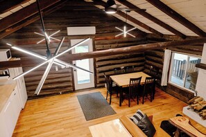 A log cabin interior with a dining area, a sofa, and a kitchen. - Remodeled Cook Forest Cabin (Clarington)