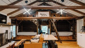 A rustic cabin interior with a loft bed, a dining table, a sofa, and a fireplace. - Remodeled Cook Forest Cabin (Clarington)