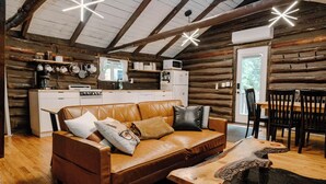 A cozy log cabin interior with a leather sofa, wooden dining table, and rustic decor. - Remodeled Cook Forest Cabin (Clarington)