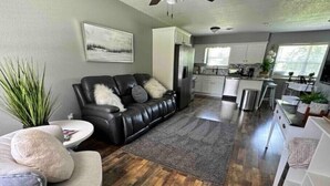 Eine moderne Küche mit weißen Schränken, ein Essbereich mit grauem Sofa und Holzboden.