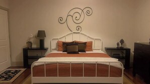 A bedroom with a white metal bed frame, a brown bedspread, and multiple pillows. There are two bedside tables with lamps and decorative items. - Lovely Condo in the Very Heart of NoDA (Charlotte)