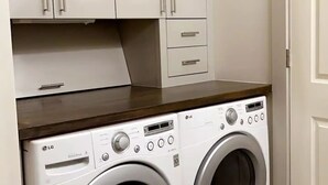 A laundry area with two LG DirectOne front-loading washing machines, white cabinets above, and a tiled floor. - Lovely Condo in the Very Heart of NoDA (Charlotte)